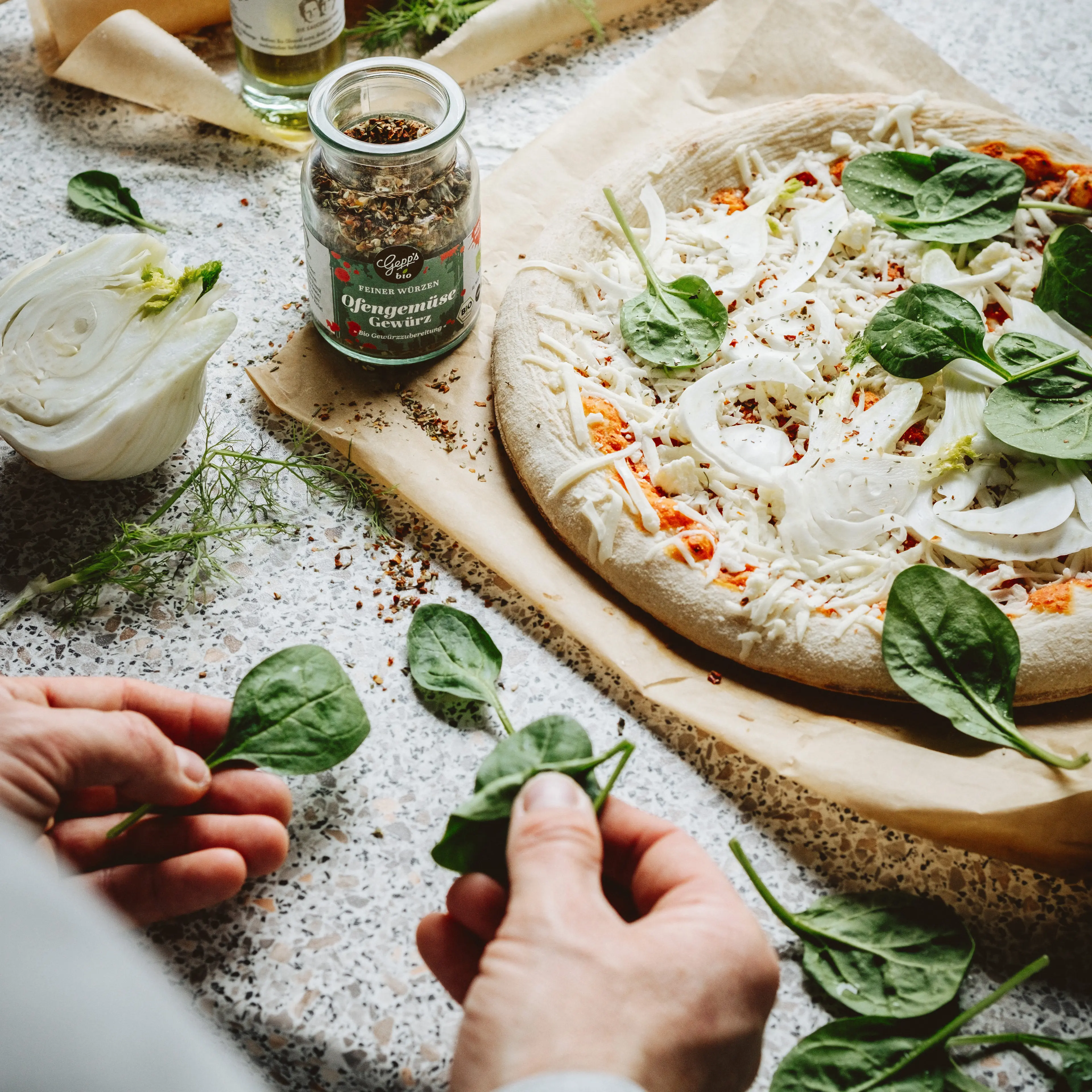 Pizza wird mit Spinat und Bio Pizzaoel vorbereitet