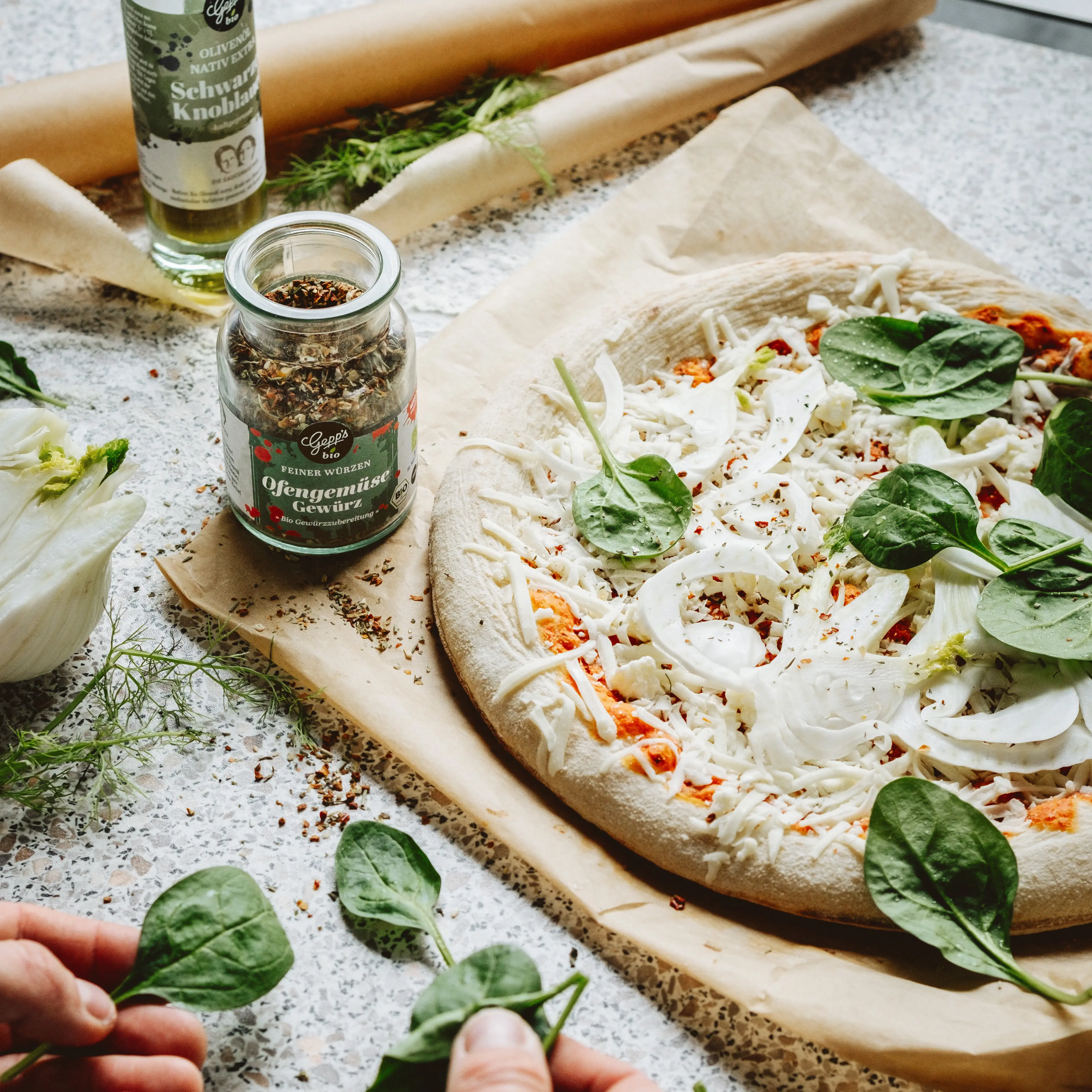 Pizza wird mit Zutaten belegt und gewuerzt